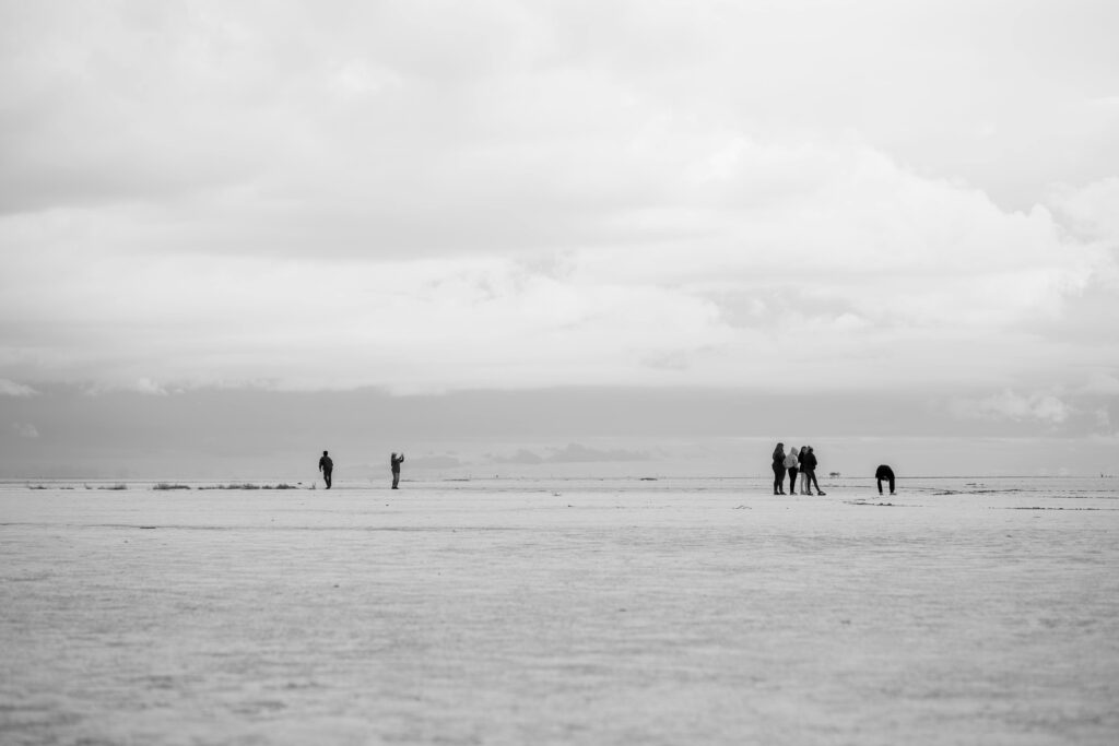 Black and white photo capturing people at vast salt flats in San José de Las Salinas, Argentina.